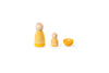 The image shows three wooden objects: two yellow cone-shaped figures with small black eyes and a floral design, and one orange half-sphere painted to resemble a slice. They are arranged in a row and are simple, colorful wooden toys for educational or decorative purposes.
