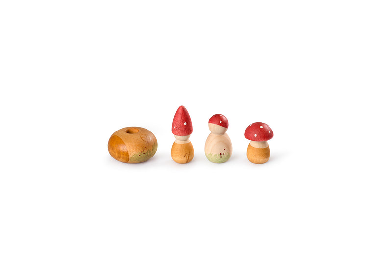 Four wooden toys resembling mushrooms are arranged in a row on a white background. The first toy is a round, flat piece with a hole in the center. The second toy has a conical red cap with white spots. The third toy has a round red cap with white spots and a small body. The fourth toy has a larger round red cap with white spots and a small body. The toys are painted with green accents at the base.