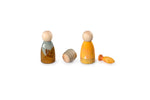 The image shows four wooden toys arranged in a row. From left to right, there is a wooden figure painted with a landscape of trees and a crescent moon, a small cylindrical wooden piece, another figure painted yellow with a white arrow, and a small wooden fish. The toys are simple and colorful, likely designed for children’s play.