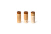 The image shows three wooden cylindrical objects with darker wooden tops. Each object has two small eyes. The objects are arranged in a row against a white background.