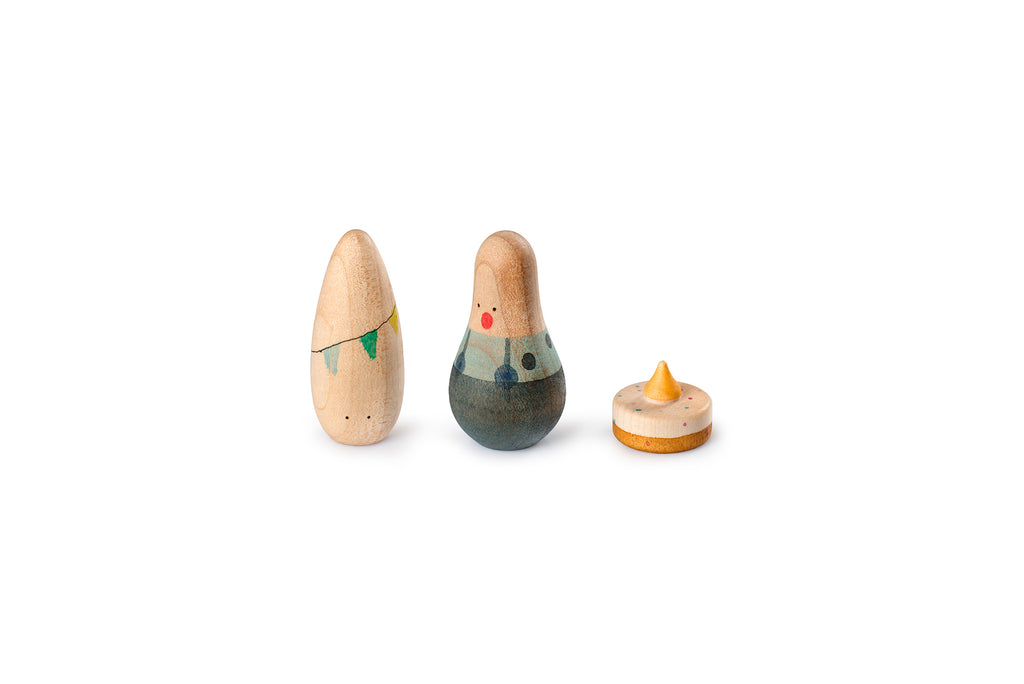 The image shows a cardboard box with multiple compartments, each holding a variety of small, colorful wooden figurines and objects. The figurines come in various shapes and sizes, resembling people, animals, and abstract forms. Inside the box, there are also two smaller boxes labeled "LUCKY," featuring a design with a bird and a banner. Additionally, there is a pencil case with a pencil and a pen, along with a couple of instruction cards displaying illustrations of the figurines.