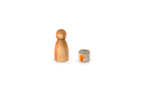 The image shows two wooden objects on a white background. The object on the left is a wooden figure with a rounded head and a cylindrical body, painted in two tones of brown with simple facial features. The object on the right is a small cylindrical piece with a design resembling a campfire on its side and a stitched pattern on the top. These handcrafted wooden toys often serve educational or decorative purposes.