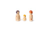 The image shows three wooden peg dolls of varying sizes. The dolls are painted with different colored dots and patterns on their heads and bodies. The largest doll on the left has purple dots and a purple pattern on its head. The smallest doll in the middle has yellow dots and a yellow pattern on its head. The medium-sized doll on the right has red dots and a red pattern on its head. The dolls are arranged in a line, with the smallest in the center.
