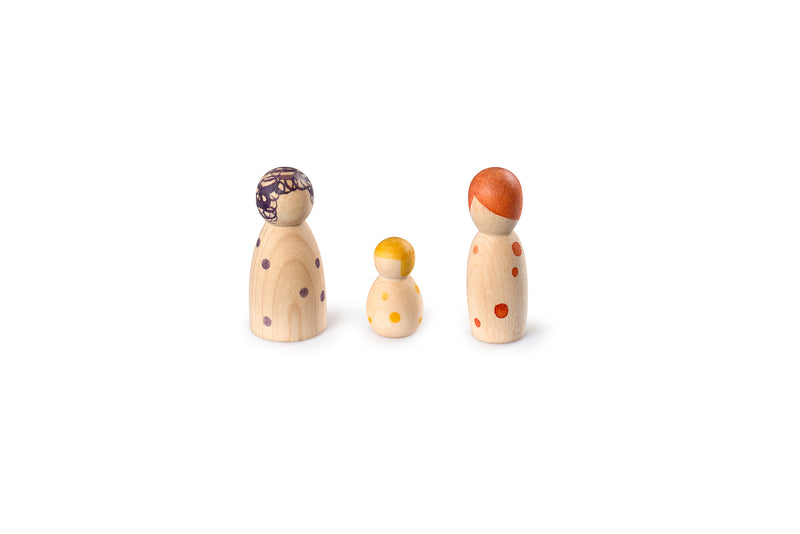 The image shows three wooden peg dolls of varying sizes. The dolls are painted with different colored dots and patterns on their heads and bodies. The largest doll on the left has purple dots and a purple pattern on its head. The smallest doll in the middle has yellow dots and a yellow pattern on its head. The medium-sized doll on the right has red dots and a red pattern on its head. The dolls are arranged in a line, with the smallest in the center.
