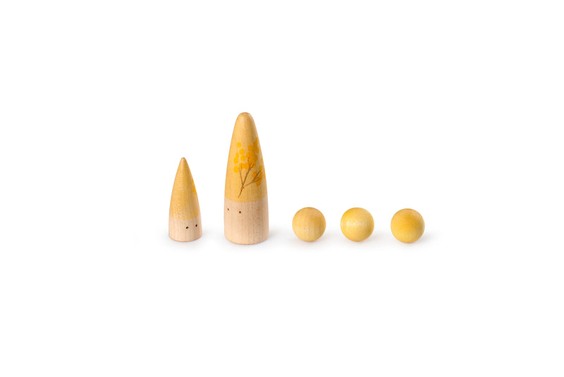 The image shows five wooden objects arranged in a row. From left to right, there are two cone-shaped figures with small black dots resembling eyes, followed by three spherical objects. The cone-shaped figures have a gradient color from natural wood at the bottom to yellow at the top, with the larger cone featuring a floral design. The spherical objects are uniformly yellow.