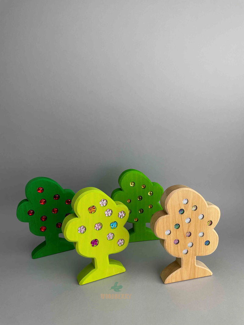 Set of 4 wooden trees with gemmed fruit from Bauspiel. Angled view of the trees standing and lined up in two rows. 