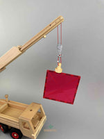 A wooden lifting magnet with red loop hanging rope by Fagus toy. A red 2x2 size Connetix magnetic tile is being lifted by the Fagus lifting magnet. All hanging on the extended arm of the Fagus mobile crane to demonstrate the magnet strength
