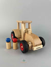 Wooden toy modern tractor by Fagus at an angle. Two wooden peg dolls (red and blue) standing right by the modern toy tractor. 