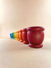 Grapat 12 mates. A set of 12 wooden mates, or cups, in rainbow colors, lined up in a row. The toy cups are arranged from red to violet, with red in the forefront, and violet fading in the distance.