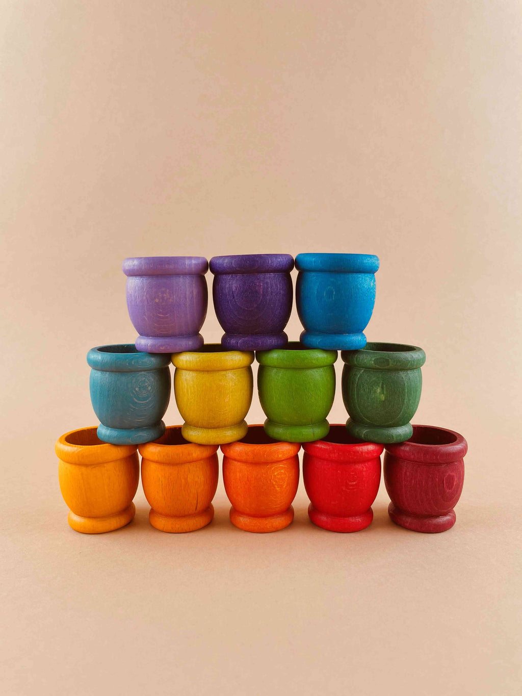 Grapat 12 mates. A set of 12 wooden mates, or cups, in rainbow colors, lined up in a row. The toy cups are arranged from red to violet, with red in the forefront, and violet fading in the distance.