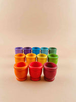 A set of 12 wooden mates, or toy cups, in rainbow colors and arranged in a row display. Three cups are in the front row (dark red to orange), 4 in the middle row (orange to light green) and 5 in the back row (green to violet). 