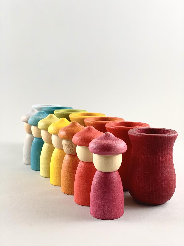Seven rainbow color Grapat Weekly Calendar cups and Nins wooden toys placed in a row.