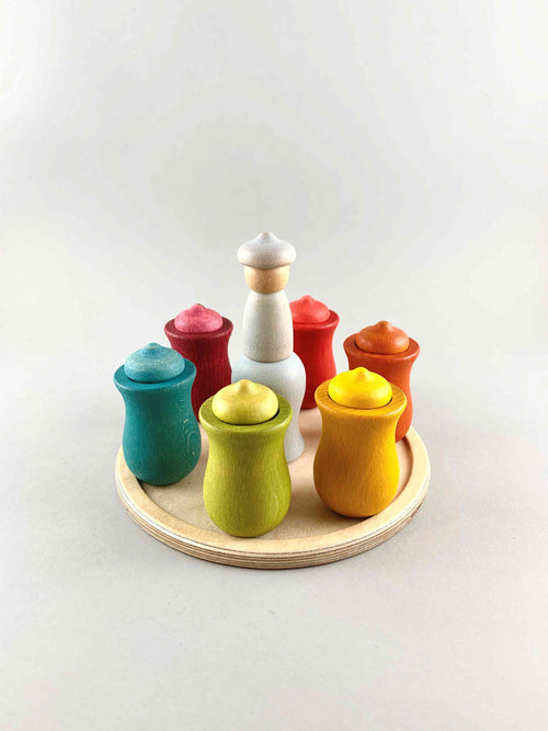 Seven wooden toy cups with special Grapat Nin peg people of different colors placed on a wooden tray. Each color represents each day of the week.