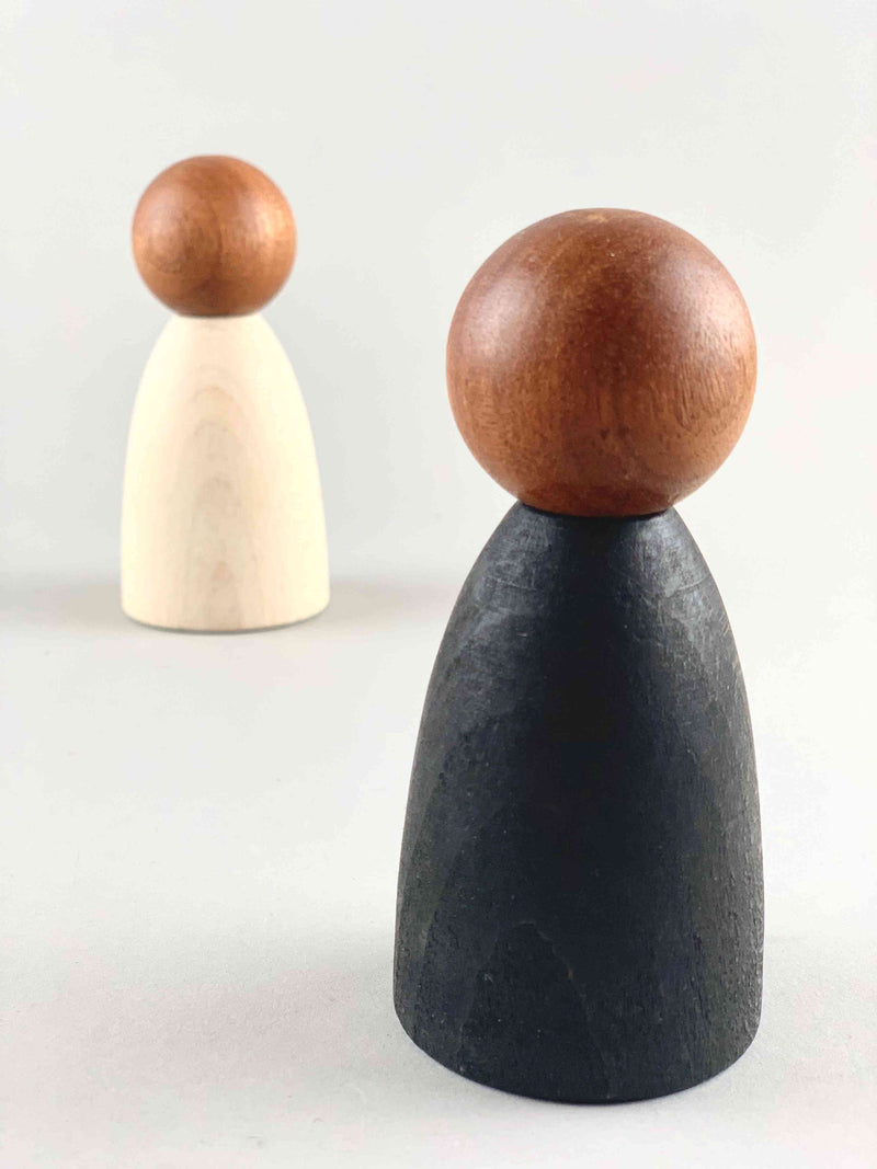 Two oversized dark wood tone Grapat Nins wooden toy figures in black (foreground) and white (background). 