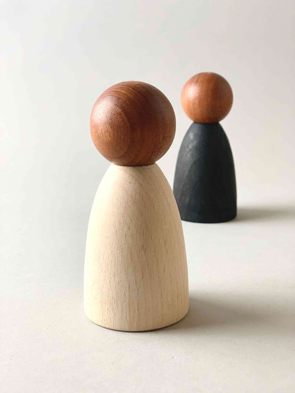 Two oversized dark wood tone Grapat Nins wooden toy figures in black (foreground) and white (background). 