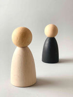 Two oversized light wood tone Grapat Nins wooden toy figures in white (foreground) and black (background).