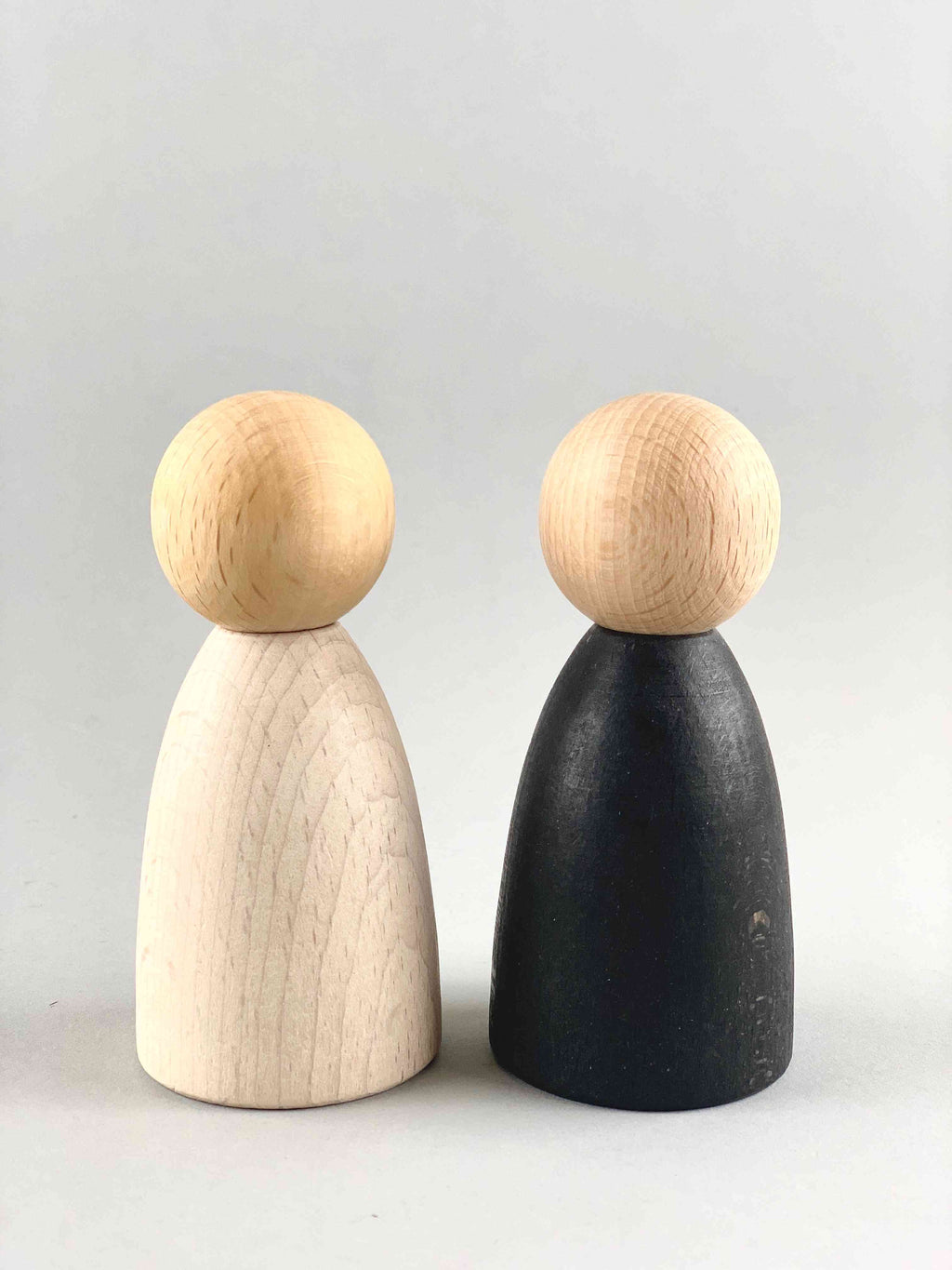 Two oversized light wood tone Grapat Nins wooden toy figures in white (foreground) and black (background).