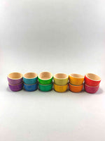 A set of rainbow colored wooden bowls nested inside each other. Six stacks of two bowls in matching color hues.