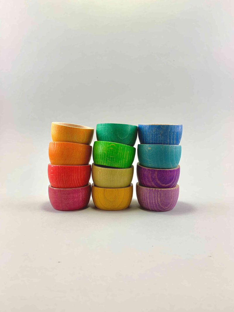 A set of 12 wooden bowls in rainbow color nested inside each other. Three stacks of 4 bowls each. 