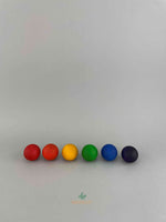 Six large wooden balls by Grapat lined up in a row: from left to right: red, orange, yellow, green, blue, purple