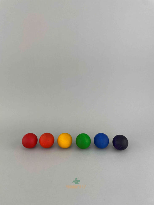 Six large wooden balls by Grapat lined up in a row: from left to right: red, orange, yellow, green, blue, purple