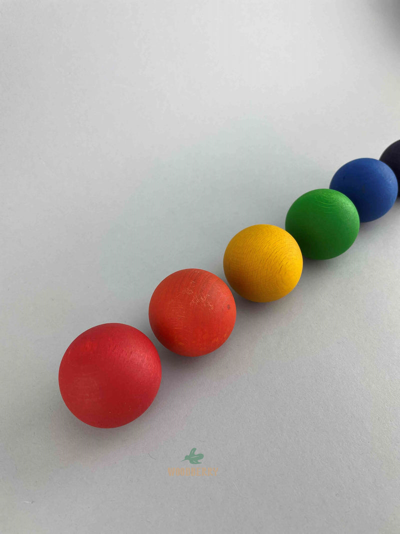 Six large colorful wooden balls from Grapat lined in a row arranged by warmer to cooler colors. 