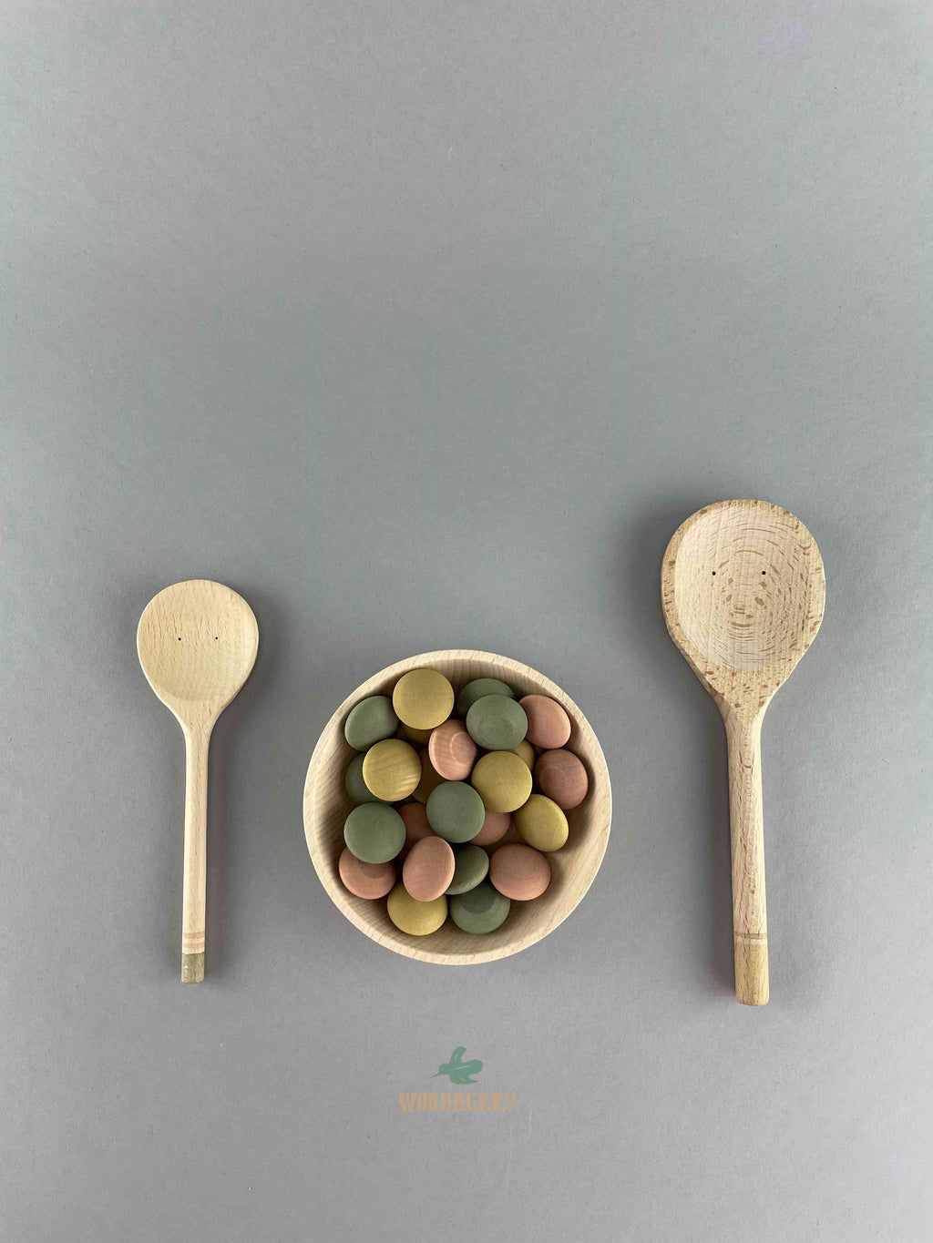 Grapat Yummy spoon and bowl set filled with natural pastel colored wooden pieces on a grey background.