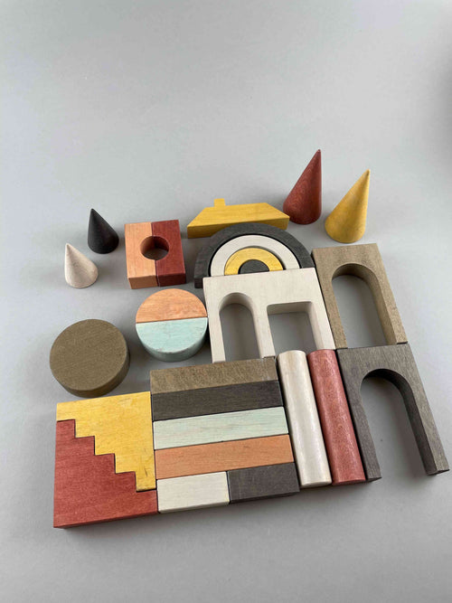 Architectural blocks. A wooden blocks set by Minmin Copenhagen. In earthy tones including beige, dark gray, brick red, pale mint green, ash and highlighted with mustard yellow. This set features four cones and arches, rainbow arches, circles, steps and many pillars. Lay out in a flat display. Total 27 pieces