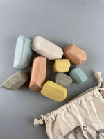 Wooden balancing stones toy by Minmin Copenhagen. A pastel set of 9 balancing stones pouring from the stamped draw string bag in the lower right corner.