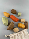 Wooden balancing stones toy by Minmin Copenhagen. An Earthy set of 9 balancing stones pouring from the stamped draw string bag in the lower right corner
