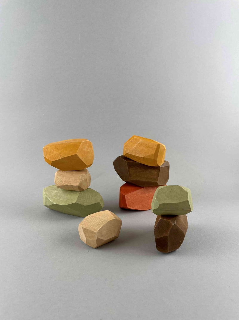 Wooden balancing stone 9 pieces Earthy set in 4 stacks. 2 stacks of 3 stones in the back and one stack of two stones and a single stone at the front. The color includes brown, brick red, olive green, beige and orange yellow.  