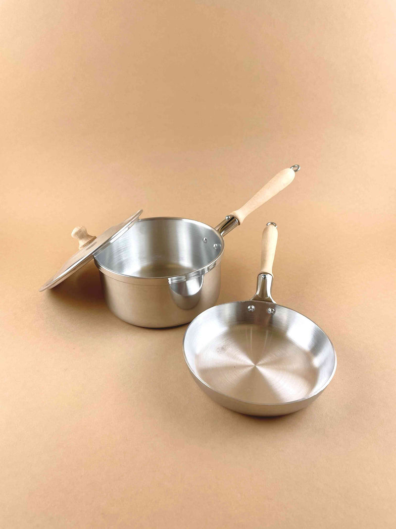 Pretend play cooking set. Two aluminum toy pots with wooden handles. Including one saucer with lid and porting spout and a saucepan. 