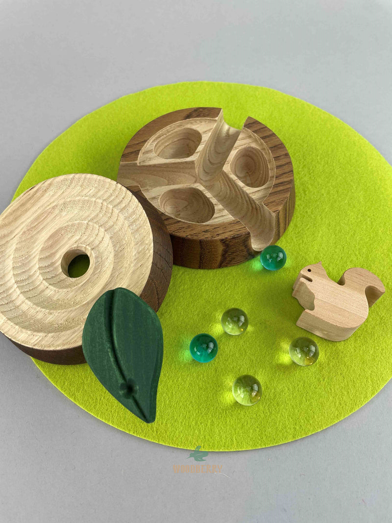 Woodberry Oak Village marble run tree stump with glass marbles and wooden squirrel figure on green felt mat. Tree stump cover is opened to reveal inside.