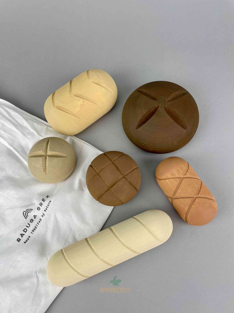 six pieces of wooden bread toy by Raduga Grez lay flat on top of the cotton draw string bag