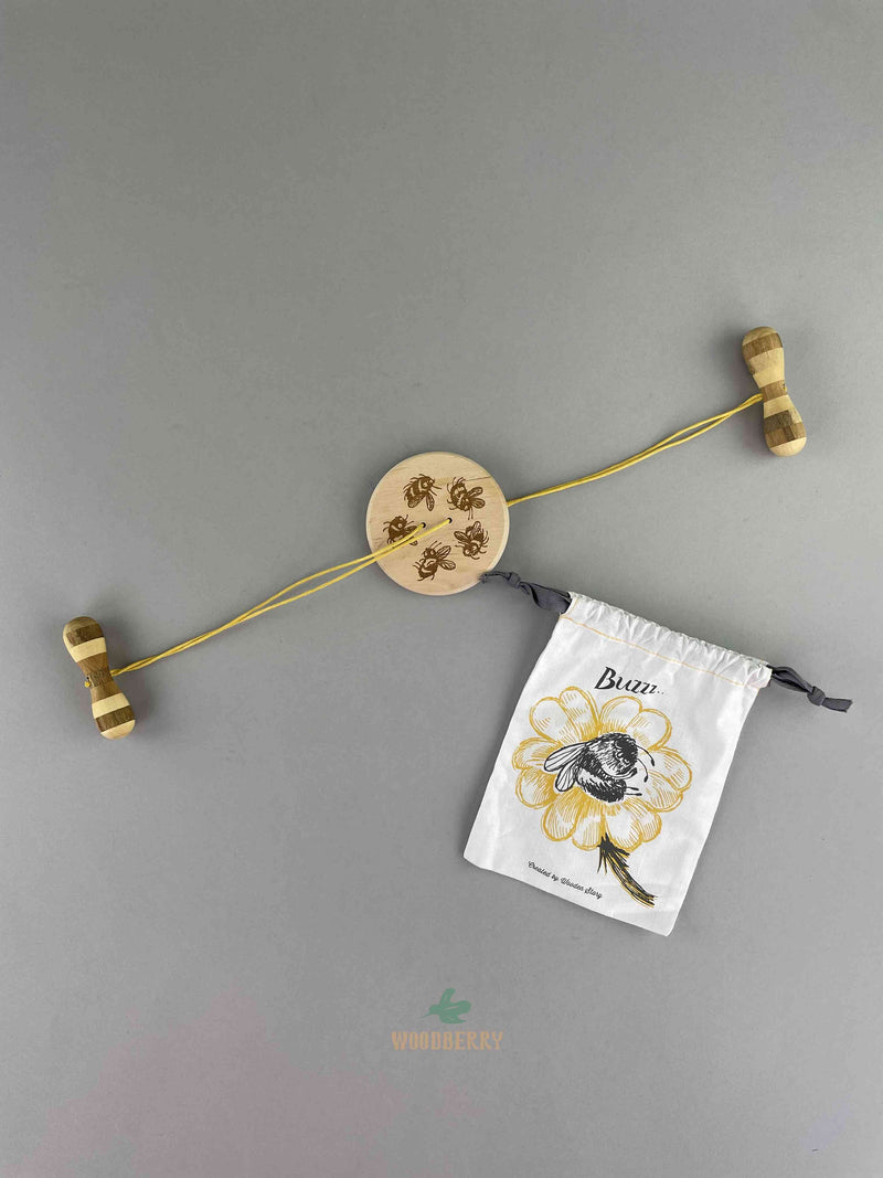 Wooden Swirling Disc. A round, 2-holes button shaped disc with bee patterns with one yellow string connected by two wooden handles. comes in a bee graphic decorated cotton string bag