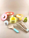 Wooden toy for pretend play and kitchen play. Wooden stock pot in red,  wooden frying pan toy in yellow. Wooden measuring cup toy in white. Wooden tong. Wooden olive oil toy. Wooden yellow mug toy. Wooden toy spoon with blue handle. By Woody Puddy Japan